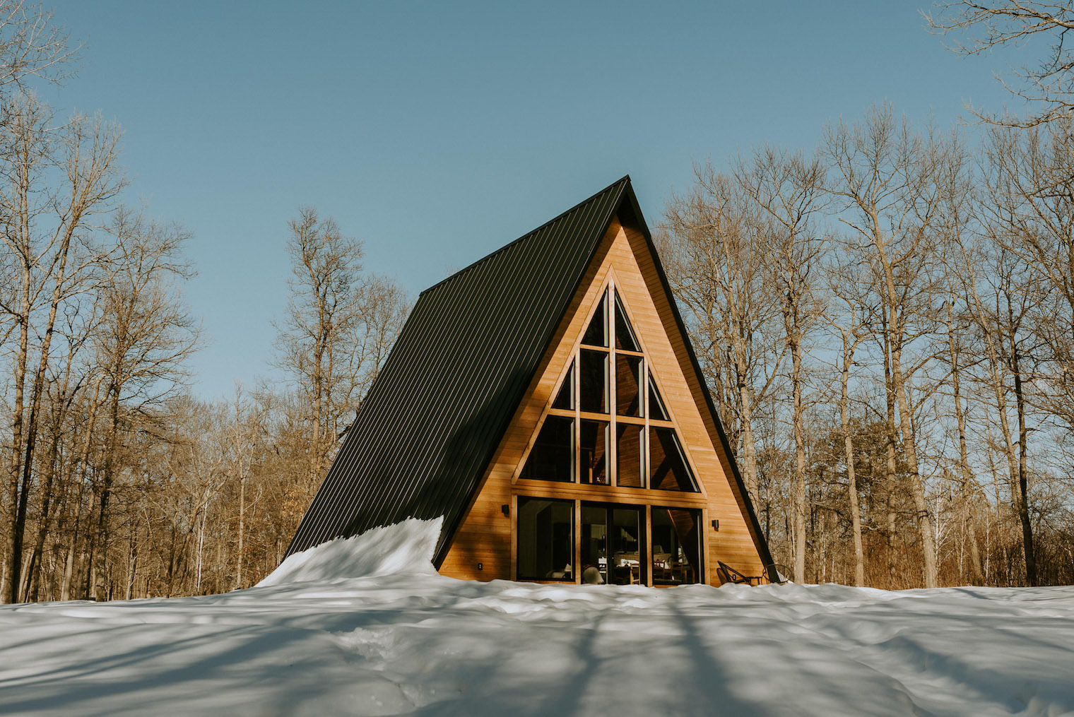 Hilhaus Aframe cabin lit by the sun in snow covered woods.